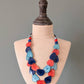 Necklace with red, blue, and orange heart-shaped beads on a mannequin bust against a gray background