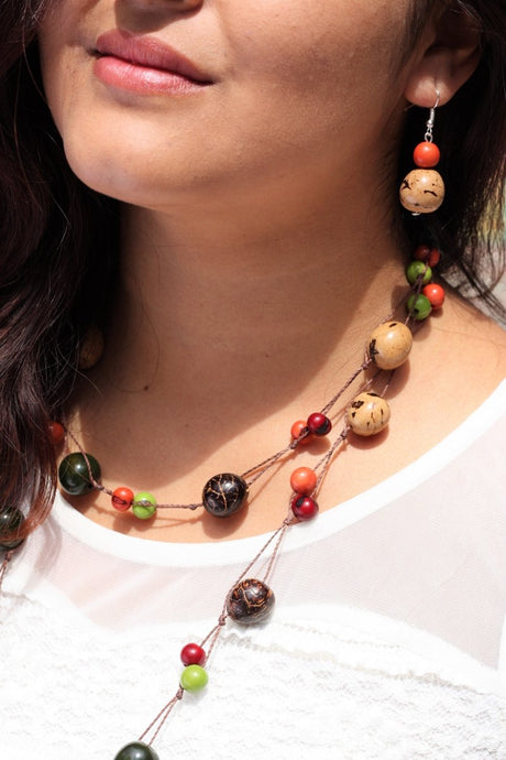 a woman wearing a long necklace that it is made of green, red and orange acai seeds and brown and cream pambil seeds